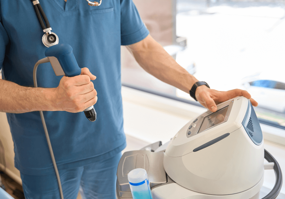 A healthcare professional in scrubs holds a medical device with a probe, operating it next to a clinical machine.